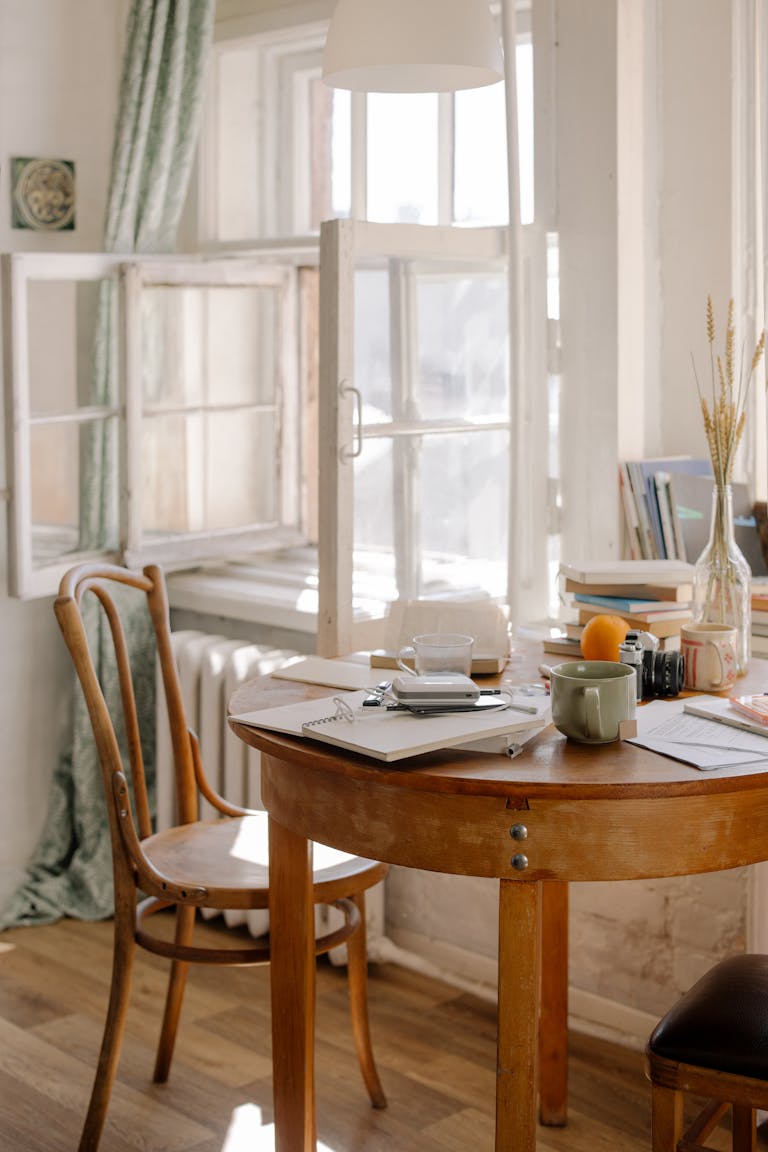 A beautifully disordered dining area with an open window, wooden table, and decorative items.