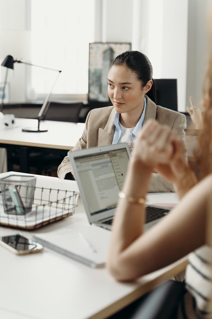 Businesswomen engage in a planning session in a modern office setting with laptops.